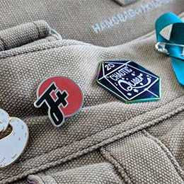 An F Plus pin sharing space on a backpack with a pin that says It Will Be Okay and a pin that says Chaotic Queer, also a teal ribbon