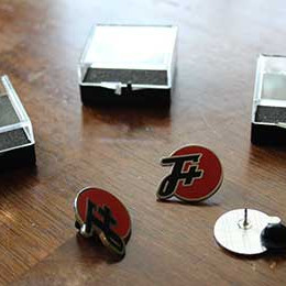 Three F Plus pins in different positions next to their cases